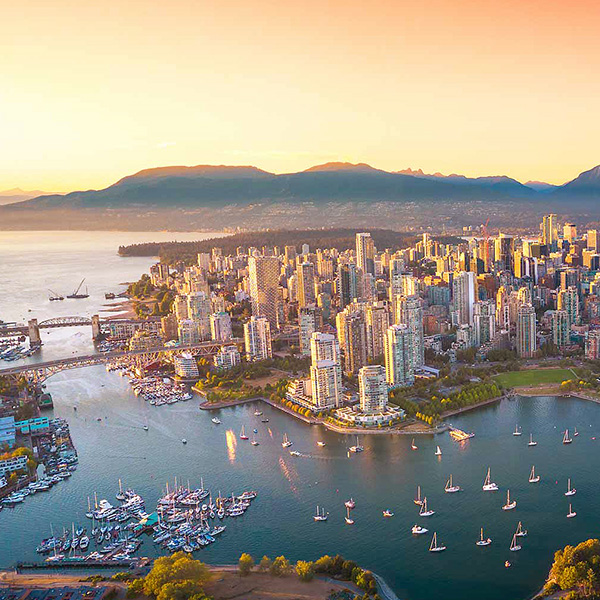 Aerial view of a coastal city skyline at sunset with sailboats in the water.