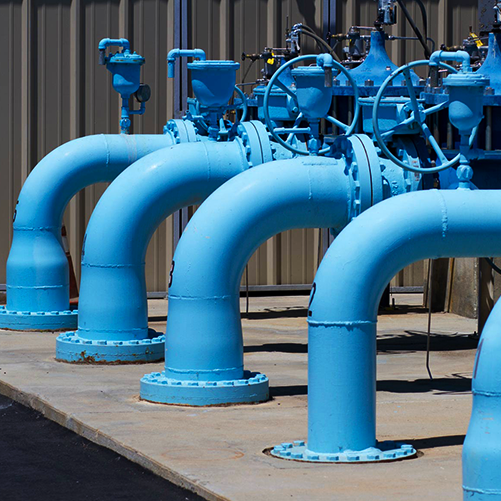 a square image of multiple large blue water line pipes that are above ground and are going into the ground, along with green overlapping border that lays on top of the image | Bentley Systems | Infrastructure Engineering Software Company a square image of multiple large blue water line pipes that are above ground and are going into the ground, along with green overlapping border that lays on top of the image