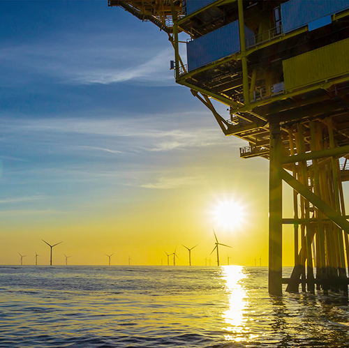 An oil rig with wind turbines in the background. | Bentley Systems | Infrastructure Engineering Software Company An oil rig with wind turbines in the background.